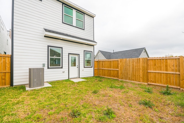 rear view of house with a fenced backyard, central AC unit, and a lawn