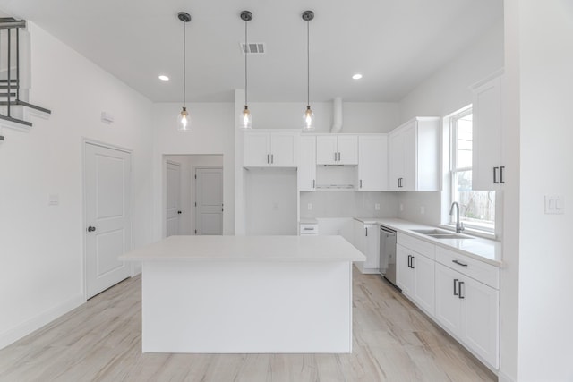 kitchen featuring visible vents, stainless steel dishwasher, white cabinetry, a kitchen island, and a sink