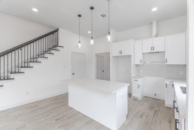 kitchen with pendant lighting, light wood finished floors, visible vents, white cabinetry, and a kitchen island