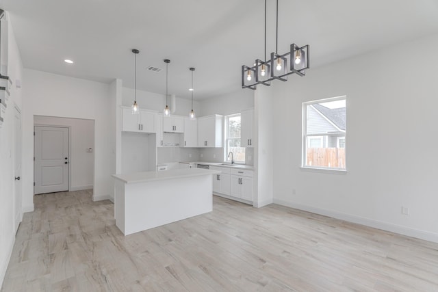 kitchen with a sink, a kitchen island, white cabinetry, and baseboards