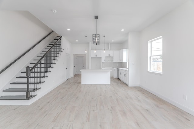 kitchen with light wood-style floors, white cabinets, a kitchen island, and baseboards