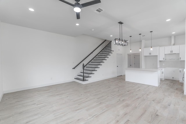 unfurnished living room with baseboards, visible vents, stairs, light wood-style floors, and ceiling fan with notable chandelier