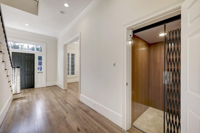 entrance foyer with light wood finished floors, baseboards, elevator, stairway, and crown molding