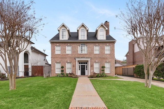 colonial house featuring brick siding, fence, and a front lawn