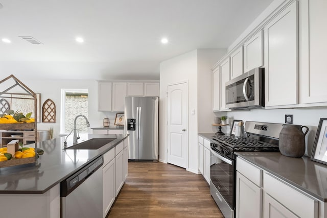 kitchen featuring stainless steel appliances, dark countertops, visible vents, and a sink