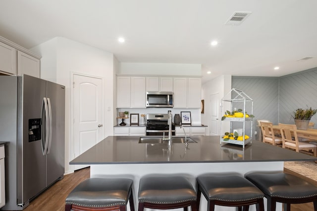 kitchen featuring a breakfast bar area, dark countertops, visible vents, appliances with stainless steel finishes, and dark wood-type flooring