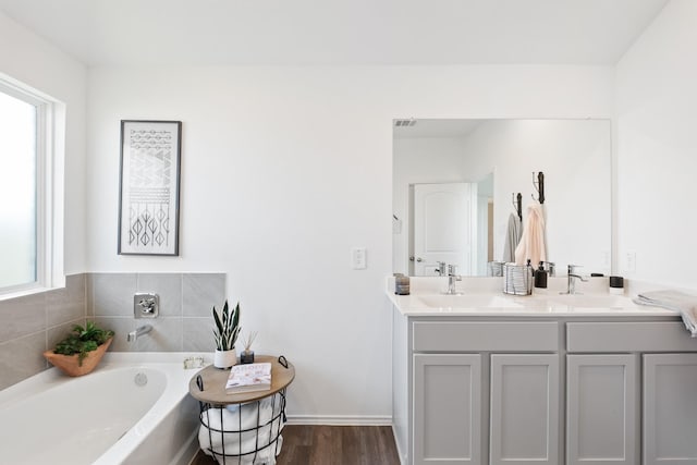 full bath featuring wood finished floors, a garden tub, a sink, and double vanity