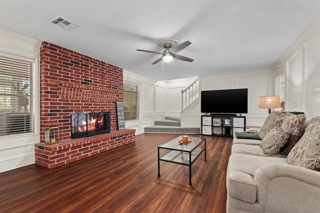 living room with a brick fireplace, wood finished floors, visible vents, and a decorative wall