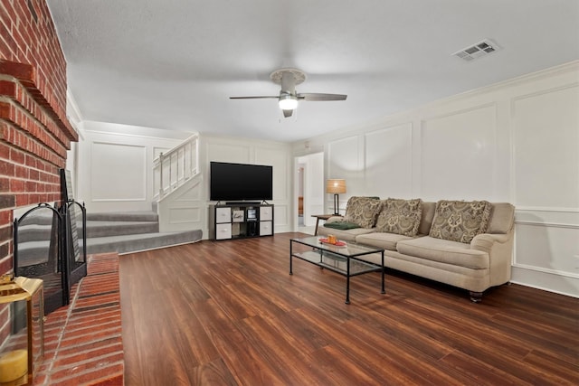 living room featuring a brick fireplace, stairs, visible vents, and a decorative wall