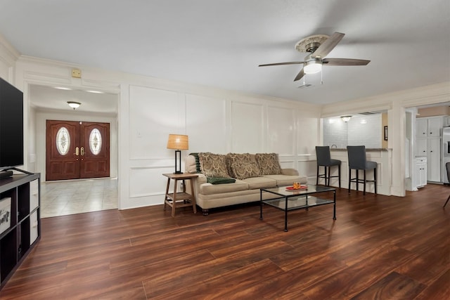 living area with a ceiling fan, a decorative wall, and wood finished floors