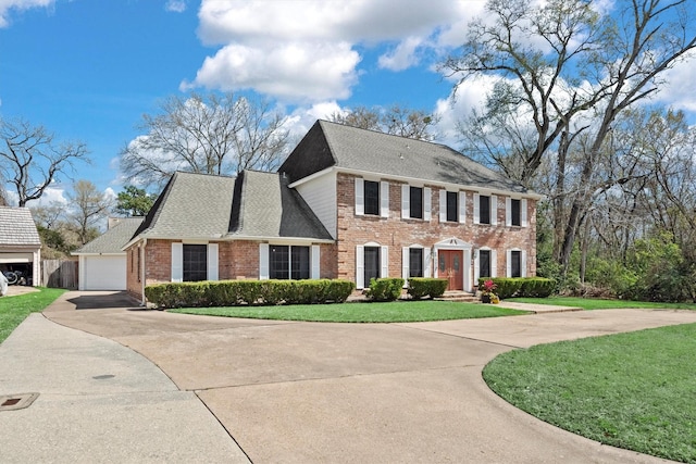 colonial home with a shingled roof, brick siding, driveway, and a front lawn