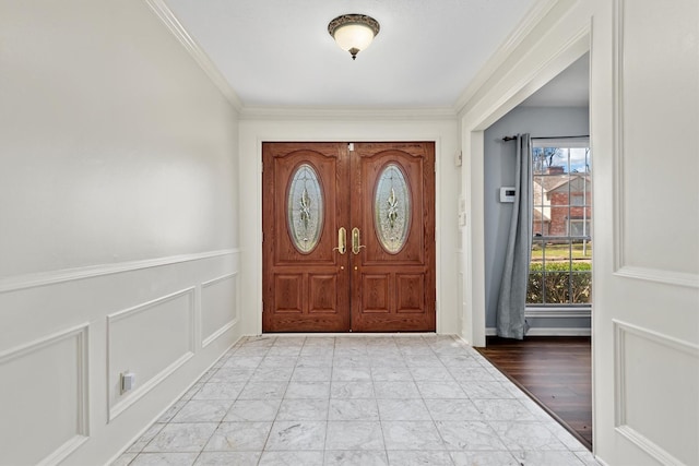 foyer with marble finish floor, ornamental molding, a decorative wall, and a wainscoted wall