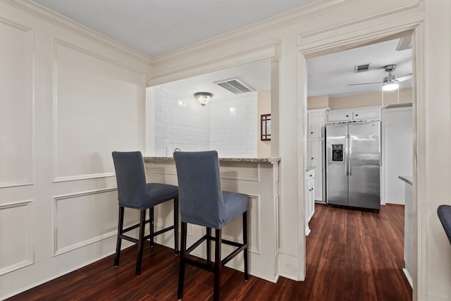 kitchen featuring dark wood-type flooring, stainless steel fridge, visible vents, and a kitchen breakfast bar