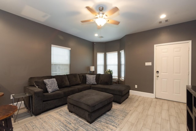 living room featuring a ceiling fan, visible vents, light wood-style flooring, and baseboards