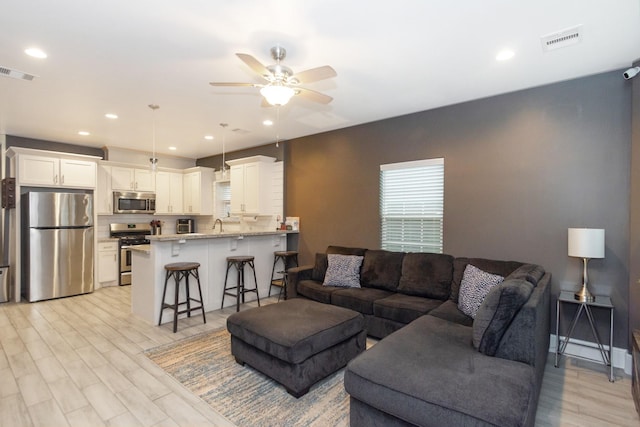 living area featuring light wood-type flooring, ceiling fan, and visible vents