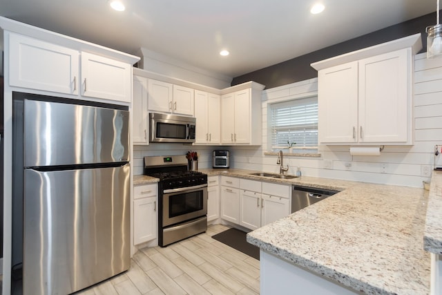 kitchen with stainless steel appliances, decorative backsplash, white cabinets, a sink, and light stone countertops