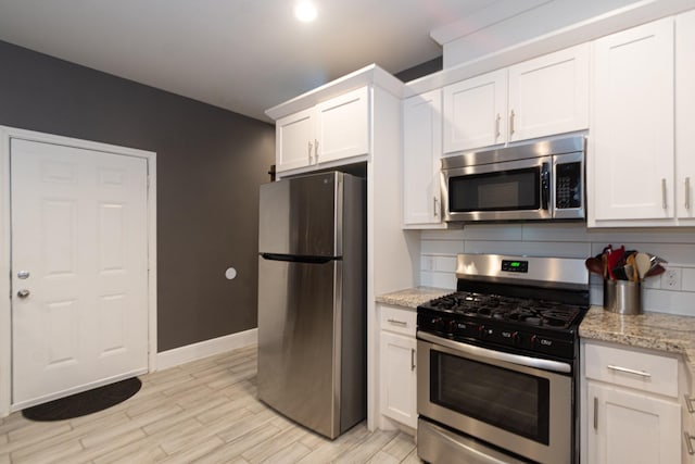 kitchen featuring stainless steel appliances, tasteful backsplash, light stone countertops, and white cabinets