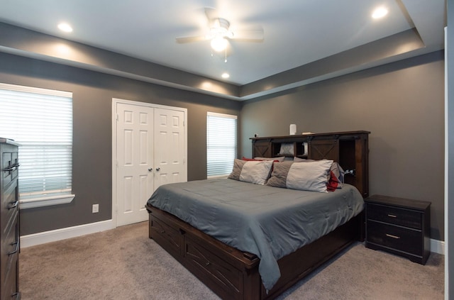 bedroom with light carpet, a tray ceiling, recessed lighting, and baseboards