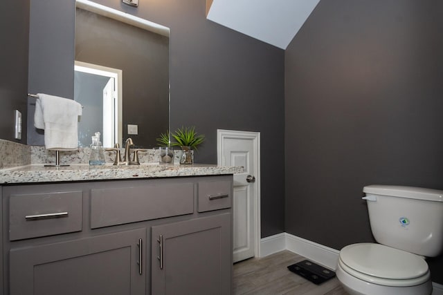 half bath with toilet, wood finished floors, vanity, baseboards, and vaulted ceiling