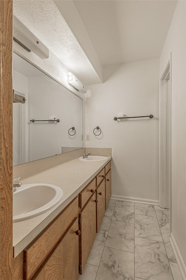 full bath with marble finish floor, double vanity, a sink, and baseboards