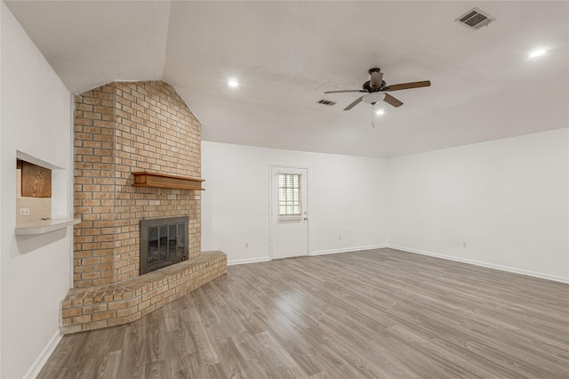 unfurnished living room with lofted ceiling, a brick fireplace, wood finished floors, and a ceiling fan