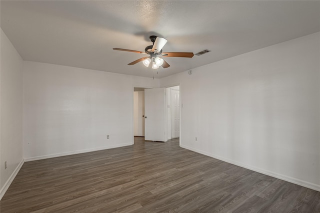 empty room featuring dark wood-style flooring, visible vents, ceiling fan, and baseboards