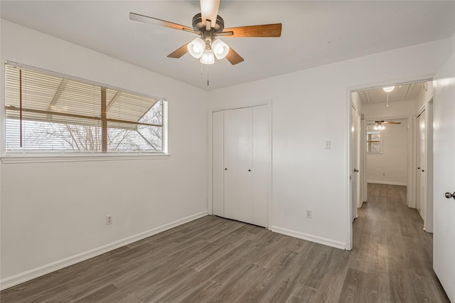 unfurnished bedroom with a closet, attic access, ceiling fan, wood finished floors, and baseboards