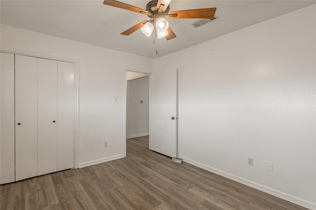 unfurnished bedroom featuring ceiling fan, wood finished floors, visible vents, baseboards, and a closet