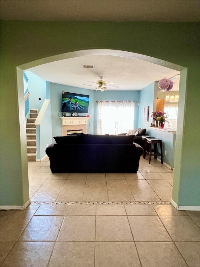 living room with ceiling fan, visible vents, baseboards, and a tile fireplace