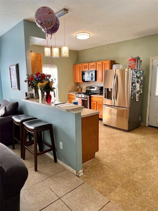 kitchen featuring a textured ceiling, a peninsula, a kitchen breakfast bar, appliances with stainless steel finishes, and pendant lighting