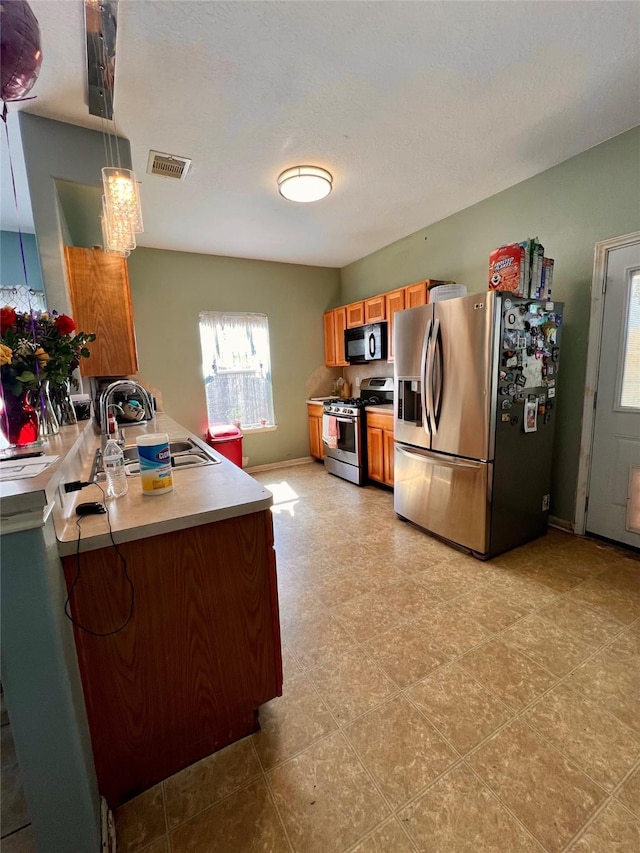 kitchen with visible vents, brown cabinetry, appliances with stainless steel finishes, a peninsula, and a sink