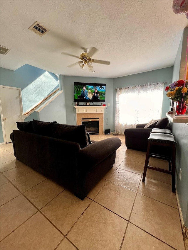 living area with ceiling fan, a fireplace, visible vents, and a textured ceiling