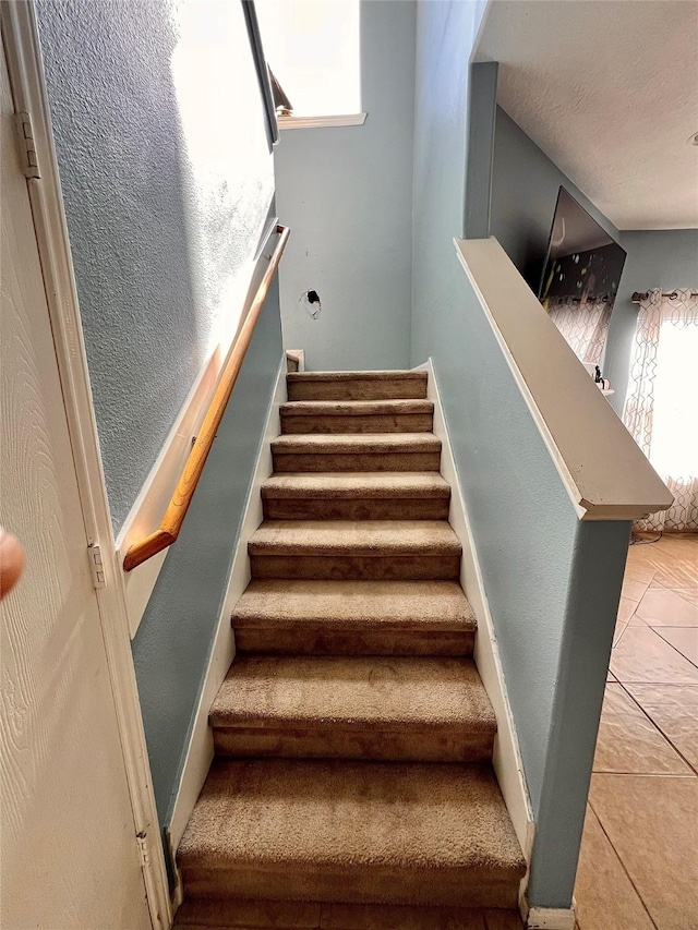 stairway with a textured ceiling and tile patterned floors