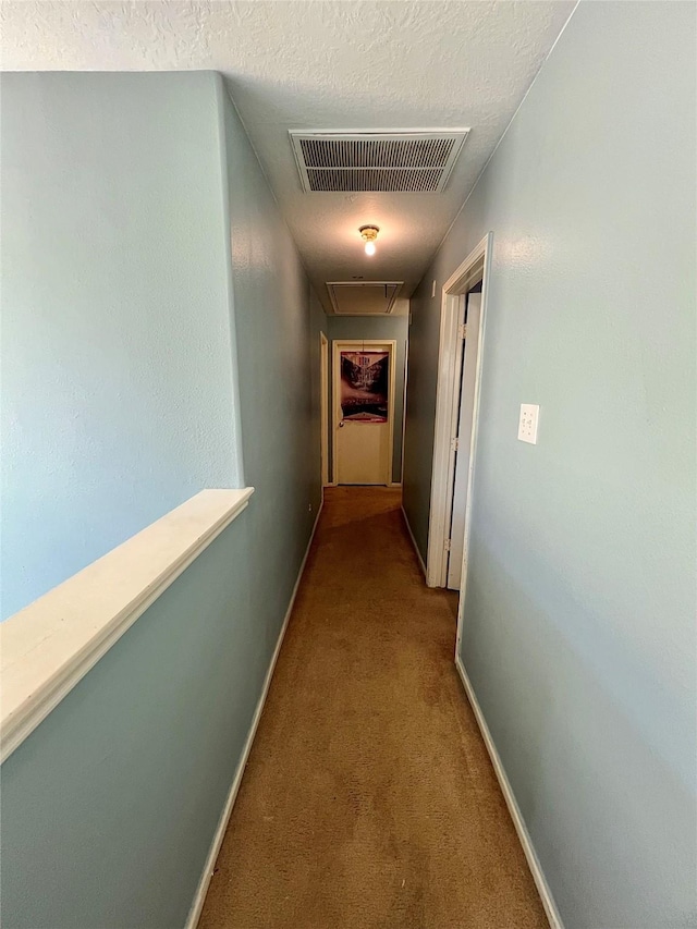 hallway with a textured ceiling, visible vents, baseboards, carpet, and attic access