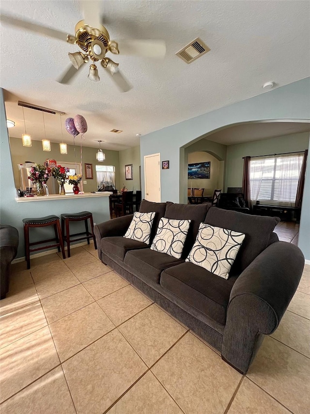 tiled living room featuring arched walkways, a textured ceiling, visible vents, and a ceiling fan