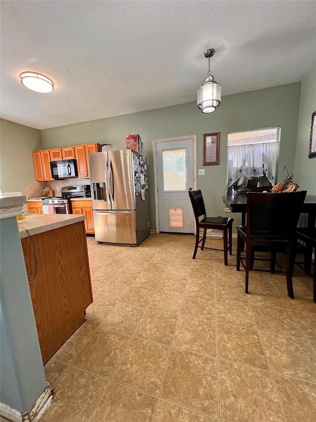 kitchen with brown cabinetry, stainless steel appliances, a textured ceiling, light countertops, and pendant lighting