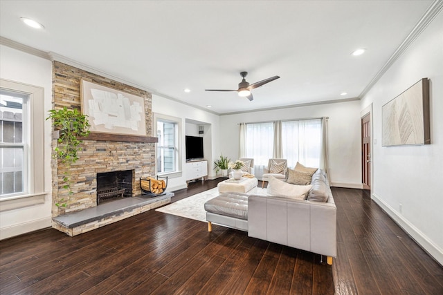 living area with crown molding, wood-type flooring, a ceiling fan, a stone fireplace, and baseboards