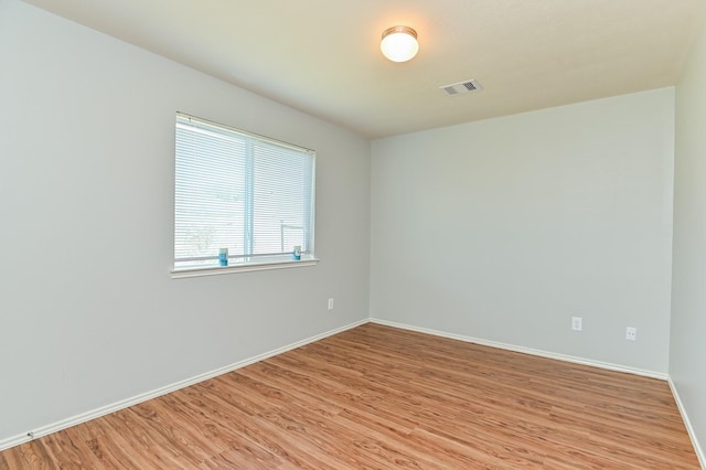 empty room featuring visible vents, light wood-type flooring, and baseboards