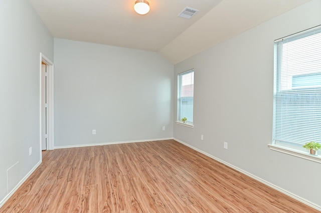 empty room featuring lofted ceiling, light wood-style floors, visible vents, and baseboards