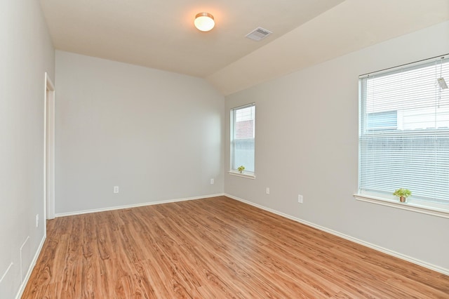 spare room featuring light wood-type flooring, visible vents, baseboards, and lofted ceiling