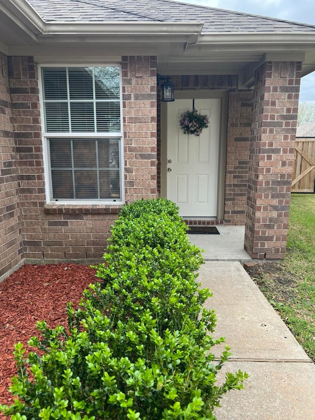 doorway to property with brick siding and roof with shingles