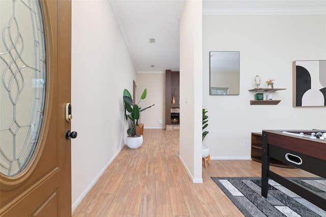 foyer with ornamental molding, light wood-type flooring, a brick fireplace, and baseboards