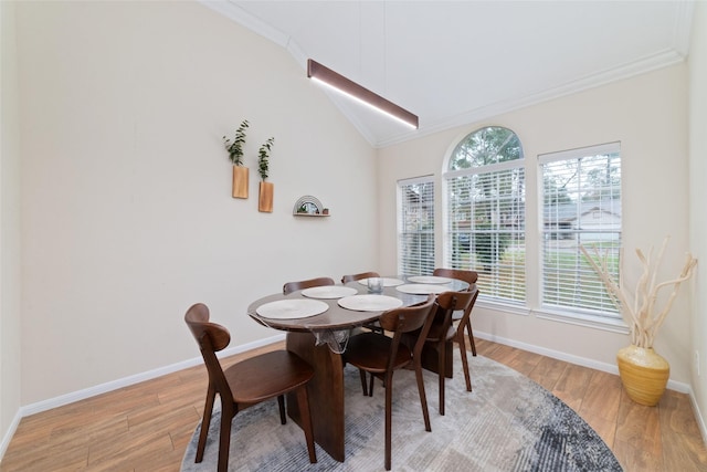 dining space with light wood-type flooring, baseboards, vaulted ceiling, and crown molding