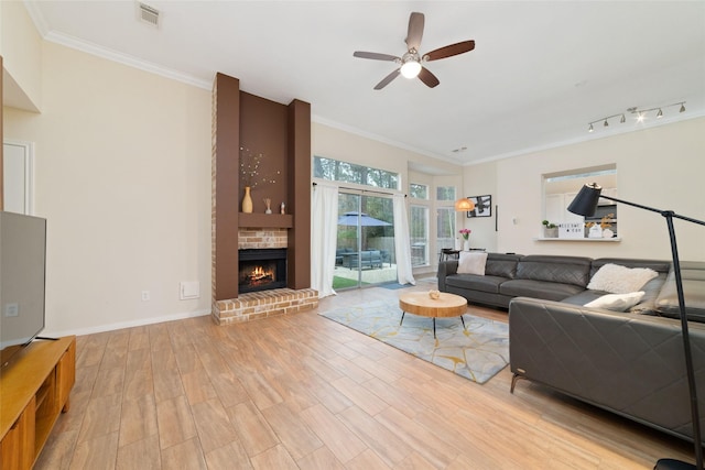 living room featuring ceiling fan, visible vents, a brick fireplace, light wood finished floors, and crown molding