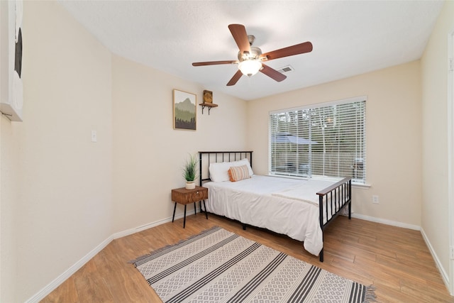 bedroom featuring ceiling fan, wood finished floors, visible vents, and baseboards