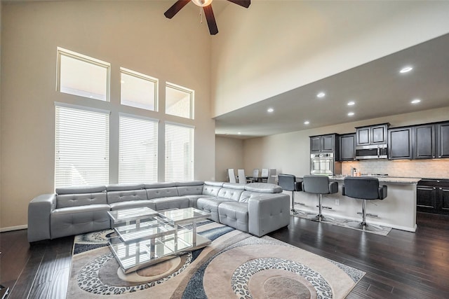 living room featuring a towering ceiling, a ceiling fan, dark wood-type flooring, and recessed lighting