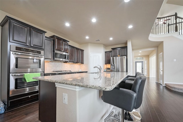 kitchen with light stone counters, stainless steel appliances, a sink, dark wood-style floors, and tasteful backsplash