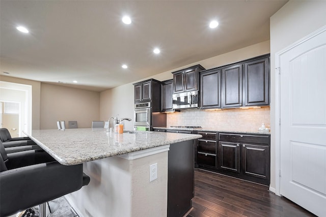 kitchen with a breakfast bar area, stainless steel appliances, dark wood-type flooring, light stone countertops, and tasteful backsplash