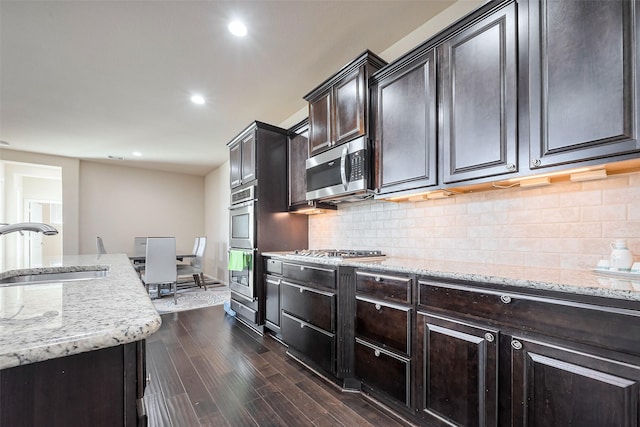 kitchen with light stone counters, dark wood-style flooring, tasteful backsplash, appliances with stainless steel finishes, and a sink