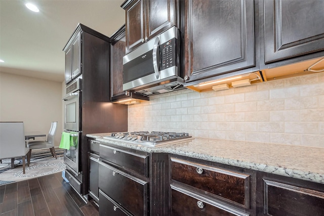 kitchen featuring stainless steel appliances, tasteful backsplash, dark wood-type flooring, dark brown cabinets, and light stone countertops